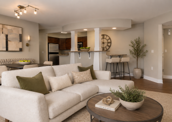 The Encore apartment homes with Modern living room with beige sofa, round coffee table, open kitchen, dining area, and neutral decor with green accents.