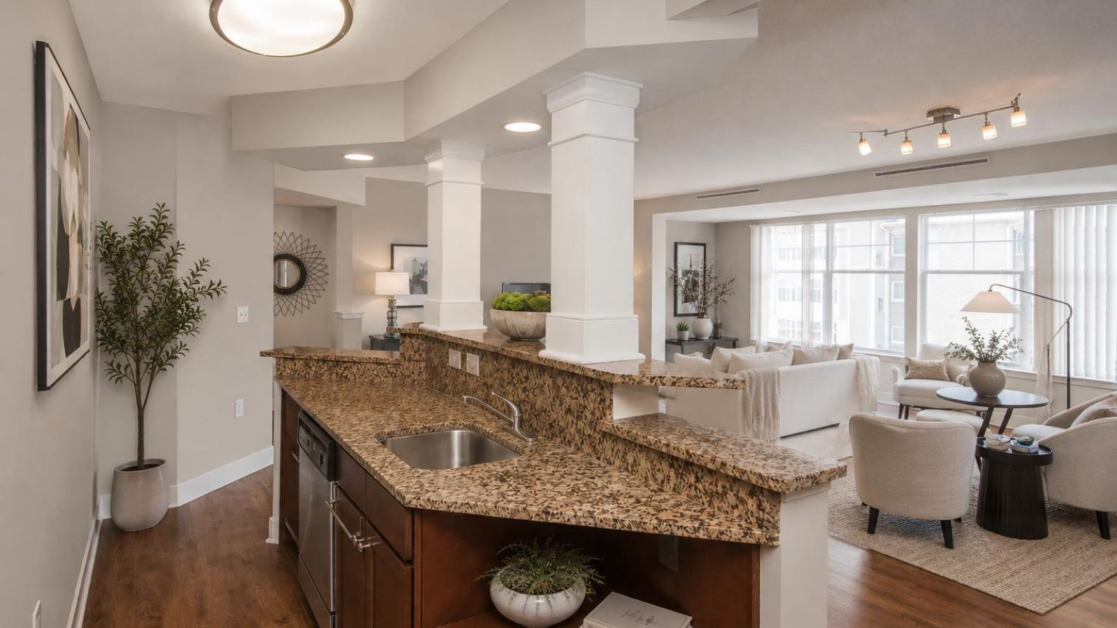 Modern kitchen and living area with white cabinets, stainless steel appliances, and a large island. Cozy seating area with a sofa and rug in the background. Bright and inviting atmosphere.
