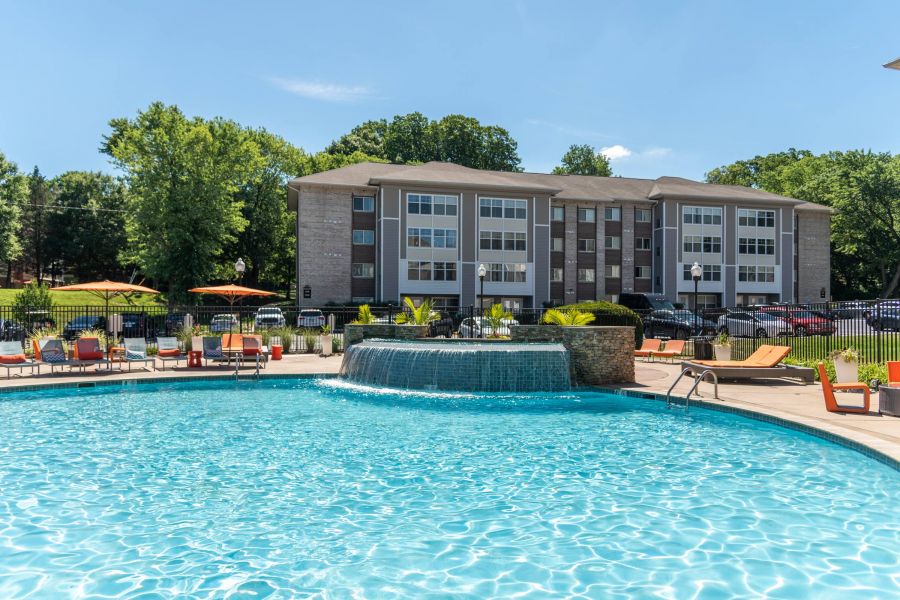 Outdoor pool with a waterfall feature, lounge chairs, and a modern apartment building in the background.