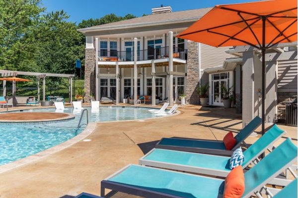 Modern apartment pool area with lounge chairs, umbrellas, and a building in the background on a sunny day.