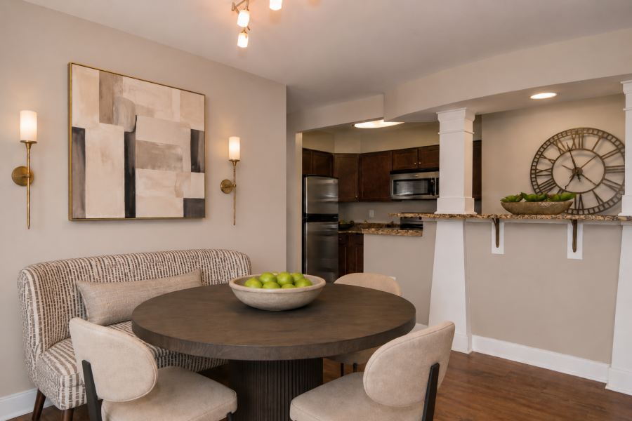 The Encore apartment homes with Modern dining area with round table, four chairs, bowl of green apples, abstract art, and view into kitchen with granite counter.