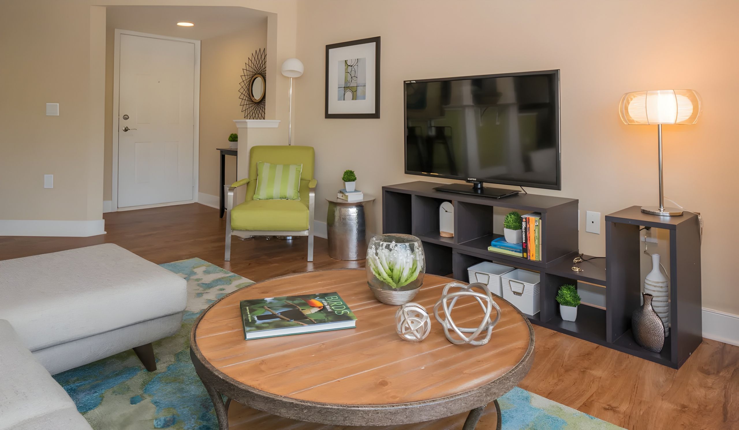 Modern living room with a TV, green chair, round coffee table, and decorative plants on wood flooring.