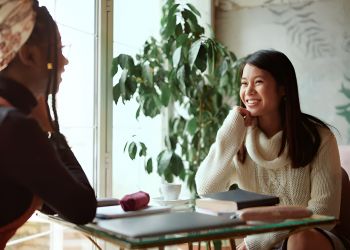 The Encore apartment homes with Two women sit at a table in a cozy cafe, smiling and talking by a window with greenery in the background.