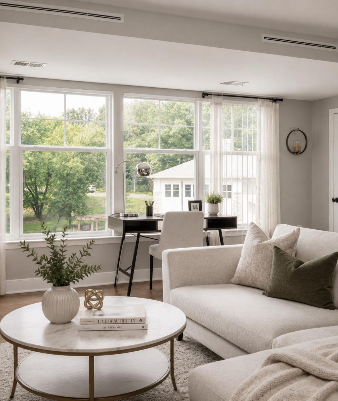 The Encore apartment homes with Bright living room with a beige sofa, round coffee table, and a desk by large windows overlooking greenery.