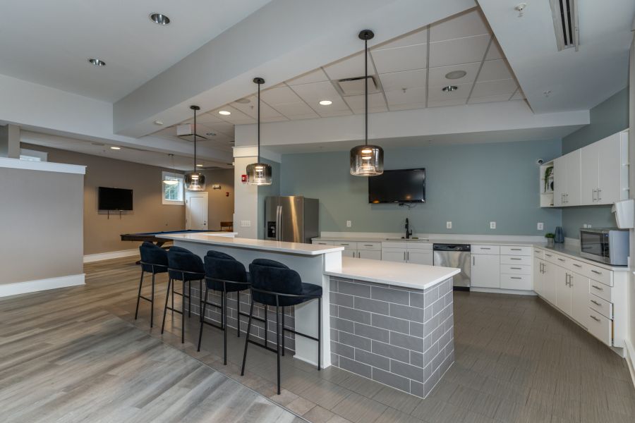 The Encore apartment homes with Modern communal kitchen with a breakfast bar, three chairs, pendant lights, and stainless steel appliances.