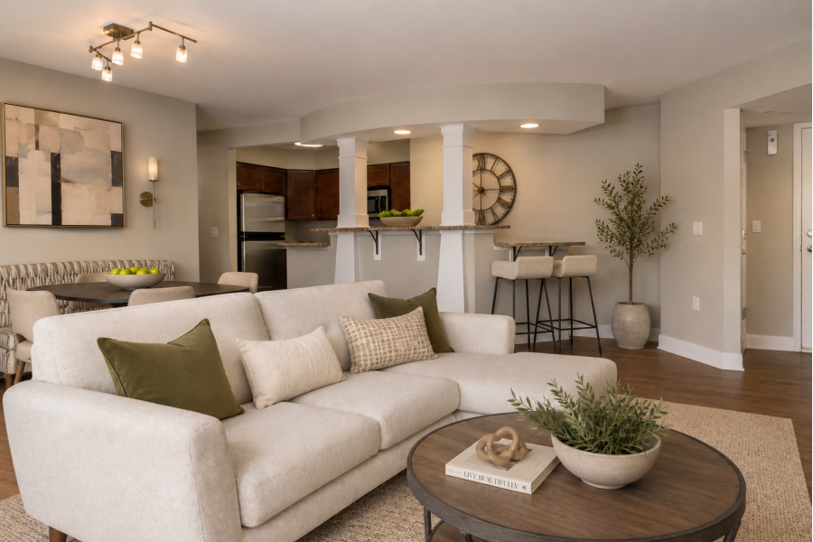 The Encore apartment homes with Modern living room with beige sofa, round coffee table, open kitchen, dining area, and neutral decor with green accents.