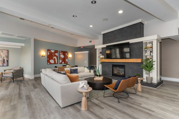 The Encore apartment homes with Modern living room with gray sectional, fireplace, wall art, and two brown chairs on light wood flooring.