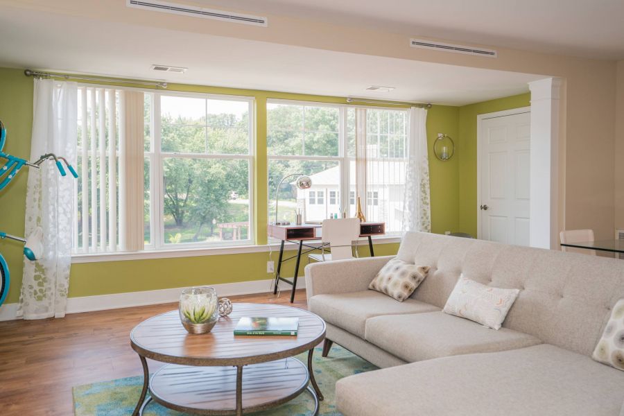 Bright living room with a beige sofa, round coffee table, and large windows letting in natural light.