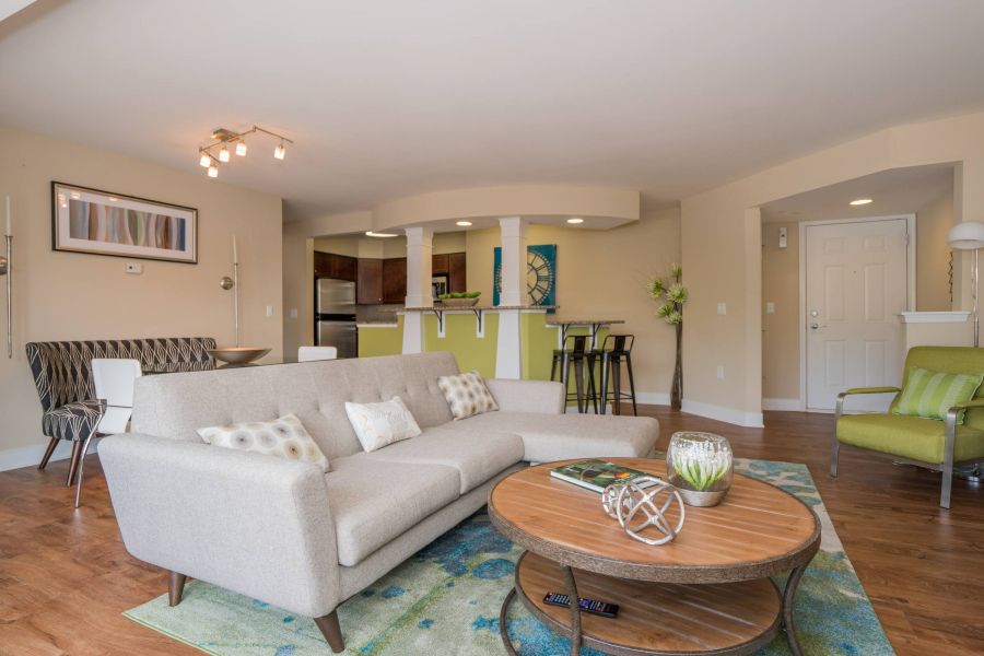 Modern living room with beige sofa, round wooden coffee table, and open kitchen in the background.