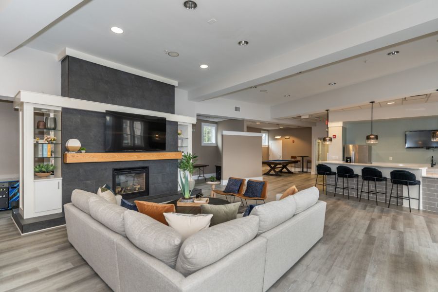 The Encore apartment homes with Modern open living room with gray sectional, wall-mounted TV, fireplace, kitchen, and bar stools in background.